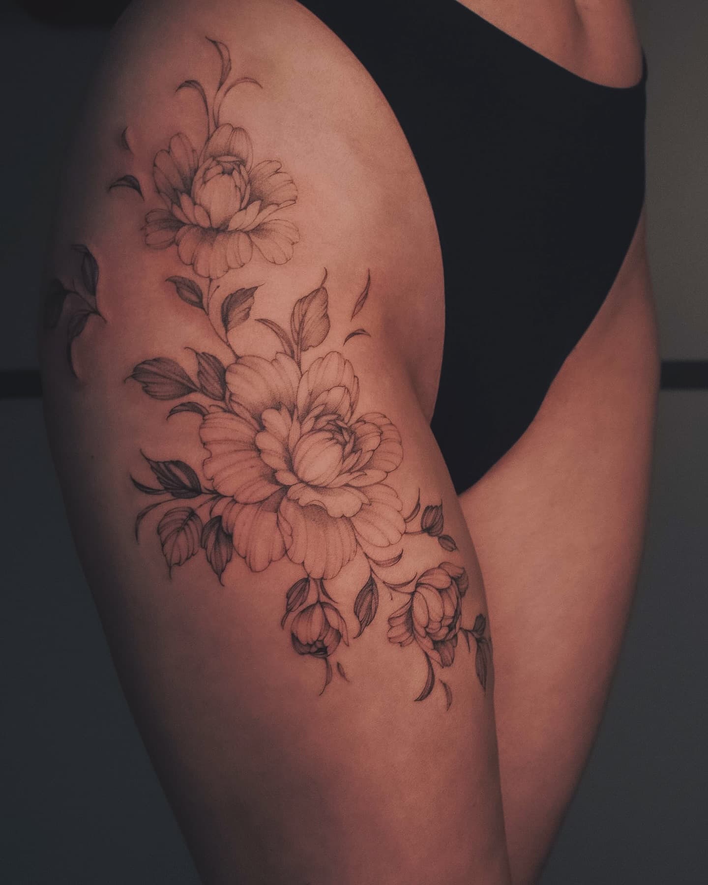 Piwonie na udzie i biodrze – tatuaż fine line