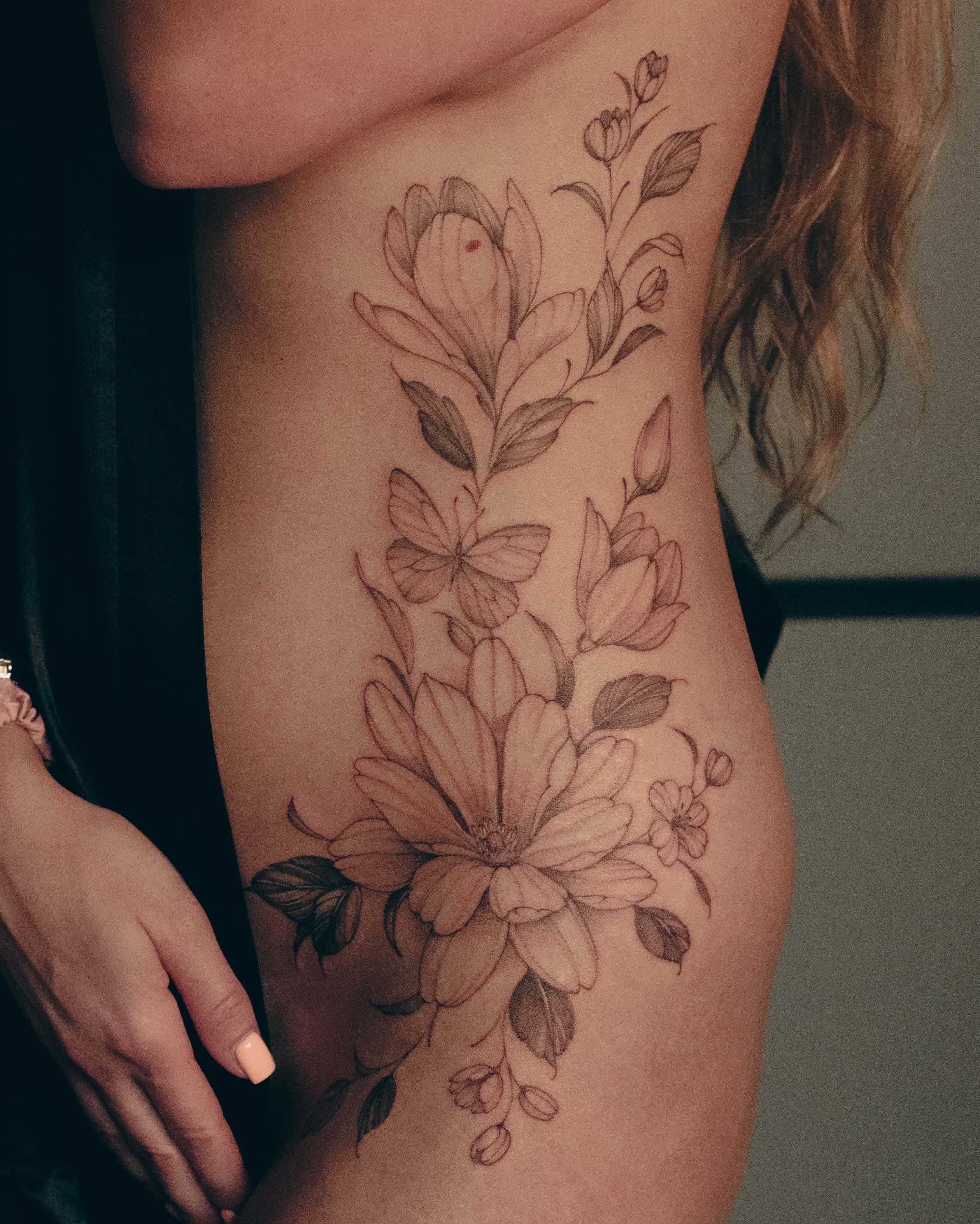 Kwiaty i motyle na boku, od żeber do biodra – tatuaż fine line
